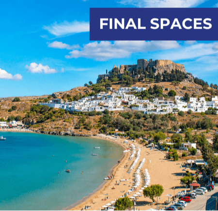 A scenic beach with golden sand, clear blue water, and a hillside village under a bright sky.