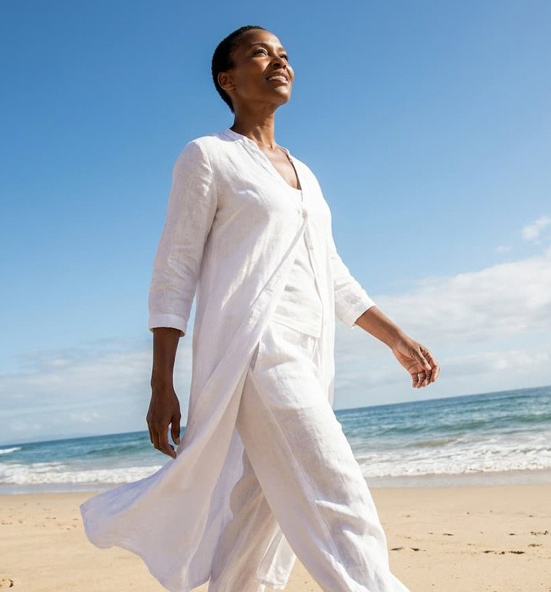 Black woman in white outfit walking on a beach