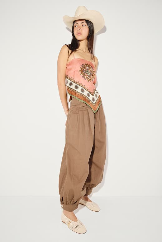 woman standing in cowboy hat with pink silk top and brown pants wearing crochet ballet flats