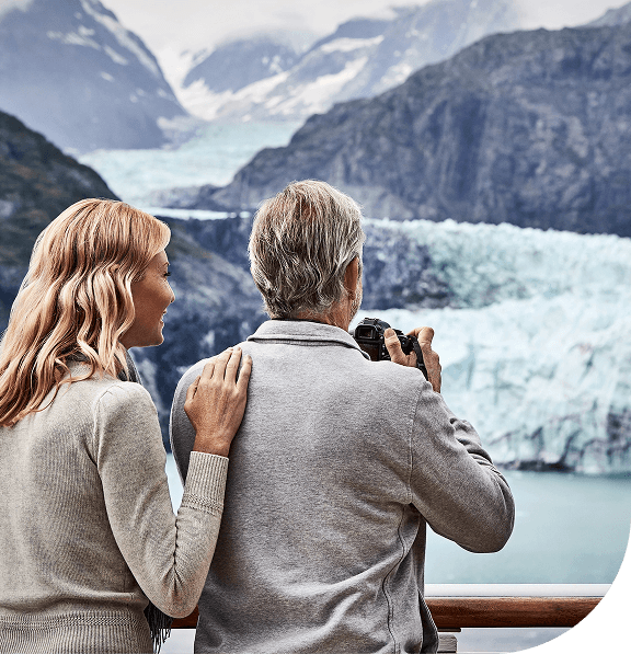 A man and woman on deck looking at a glacier and mountains.