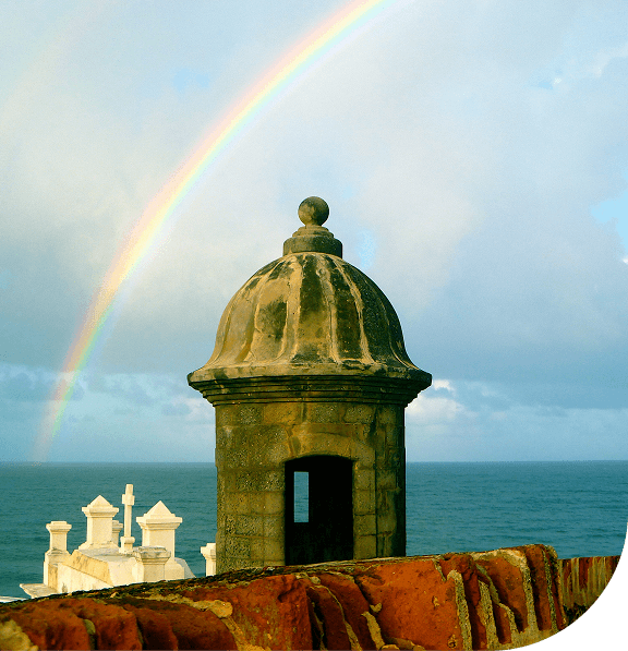 Historic stone guard tower by the ocean with a rainbow in the sky. San Juan, Puerto Rico.