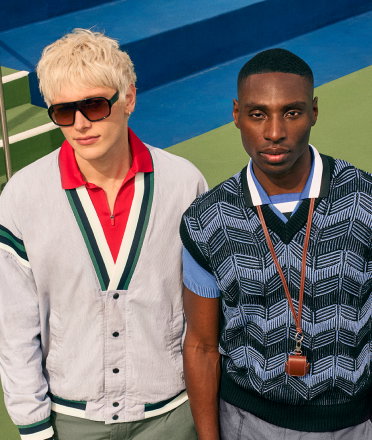 Two men standing side by side outdoors, wearing sunglasses and casual outfits. 