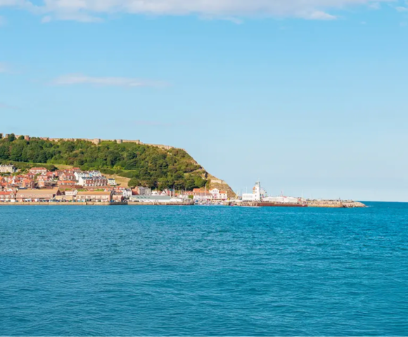 Coastal view featuring a hillside town and a lighthouse by the sea under a clear blue sky.