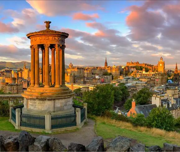 A scenic view of Edinburgh at sunset, featuring the Dugald Stewart Monument and city skyline.