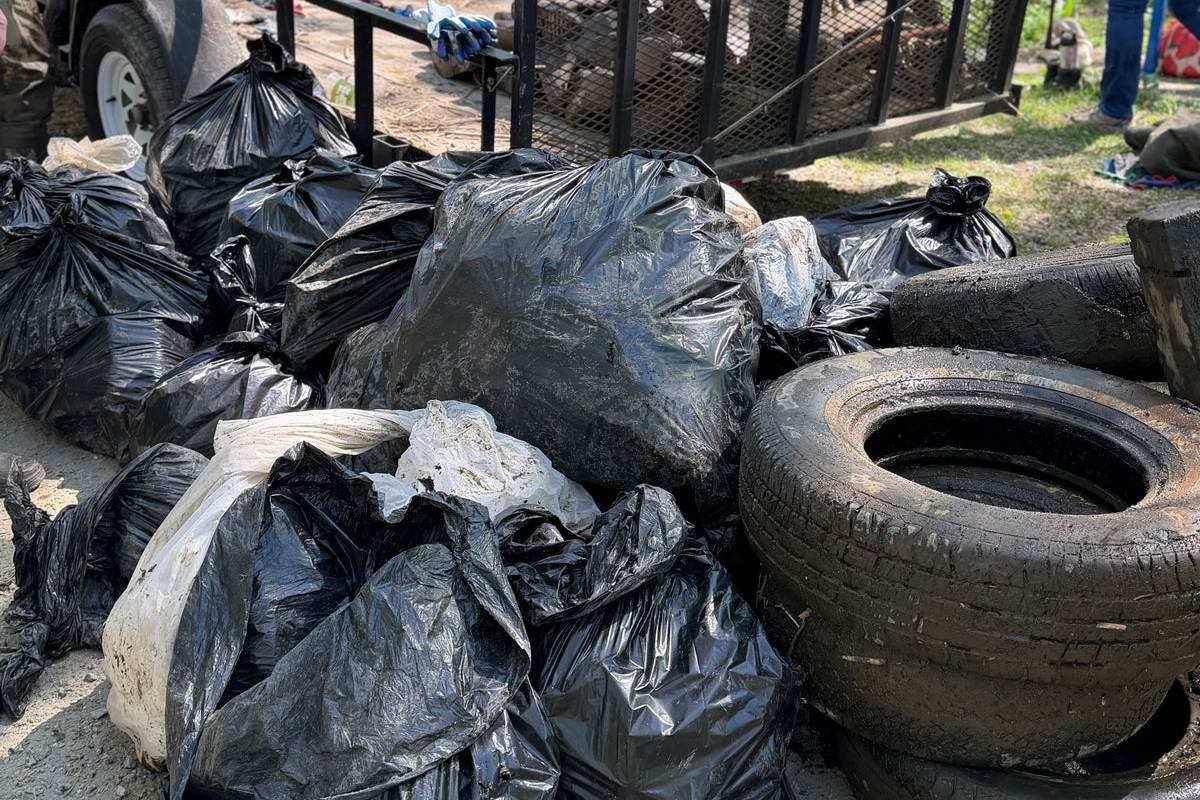 A haul of black trash bags and dumped tires pulled from the marsh, stacked beside a trailer.
