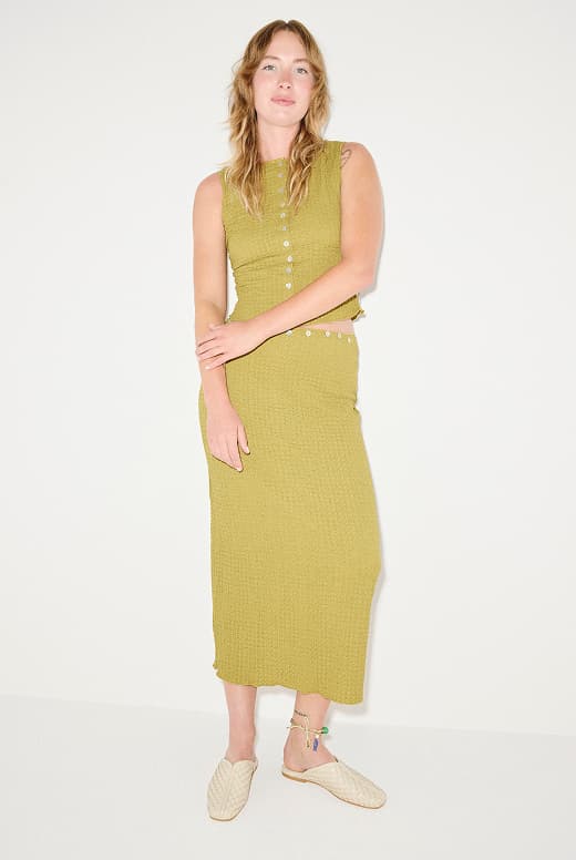 woman in olive green top and long skirt wearing vanilla colored woven slides