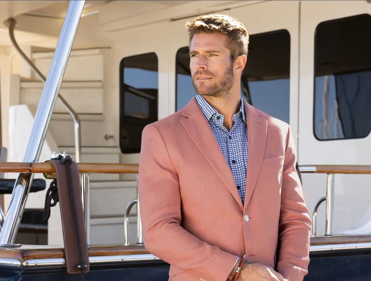 Man in a pink linen blazer standing at a yacht, closeup of face and torso.