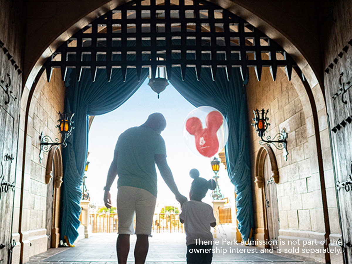 A father and son hold a Mickey balloon as they stroll under the gates of Cinderella Castle at Magic Kingdom Park.