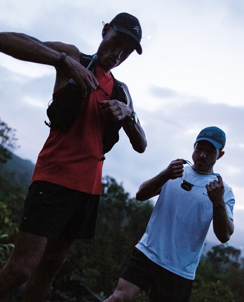 Two trail runners putting on their running vest and headlamps. 