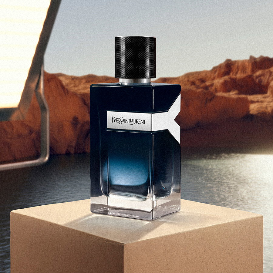 A bottle of YSL Y Eau de Parfum displayed on a stone block in front of a scenic desert canyon.