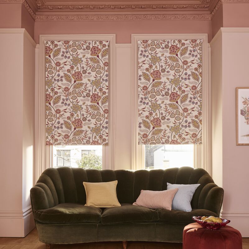 Two matching pink and white floral patterned roller blinds behind a dark velvet sofa in a dusty pink room