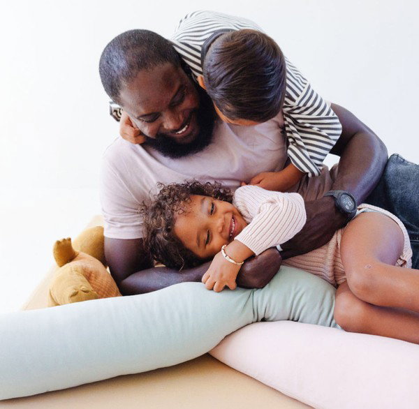 Image of a dad playing with two children on a sandcastle play mat with sage and tutu support pillows.