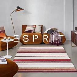 Braune Kord sofa mit bunten Kissen, ein weißer Marmor-Beistelltisch, ein gestreifter Teppich in Rot und Beige sowie eine schwarze Stehlampe.