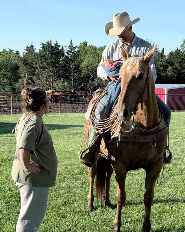 A man holding a baby while sitting on a horse.