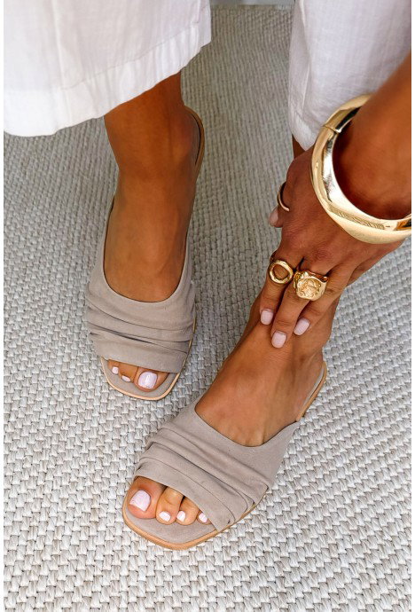 Close-up of woman's feet in beige slide sandals on a woven rug, pale-pink pedicure with gold rings and a chunky bangle