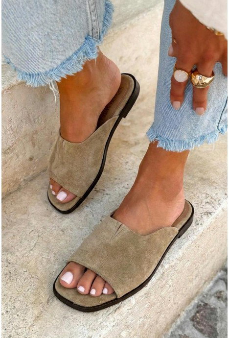 Woman's beige suede slide sandals on stone steps, white pedicure, frayed-hem denim jeans and gold rings