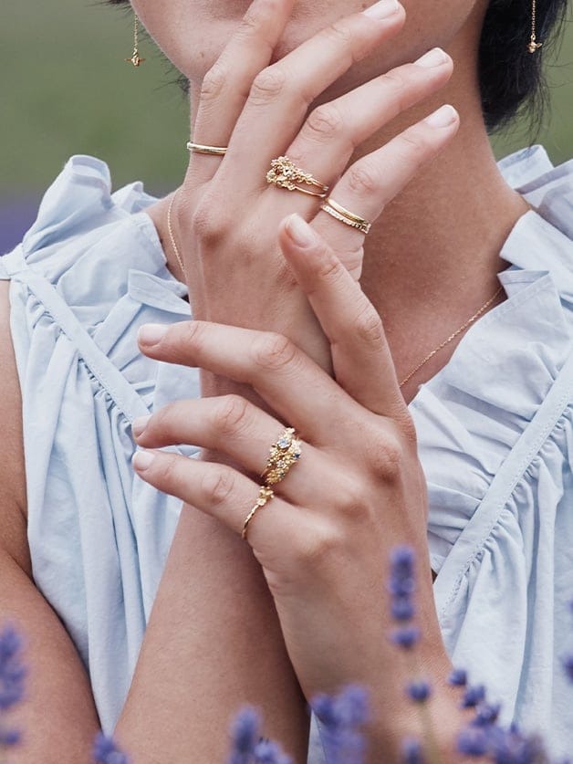Model wearing Alex Monroe stacked gold rings on both hands, featuring delicate bands and nature-inspired statement designs.
