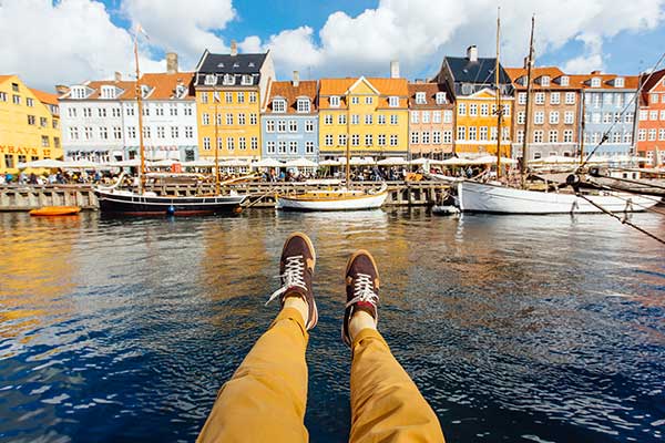 Füße über Wasser vor Hafenhäusern und Booten | Link zu AIDA