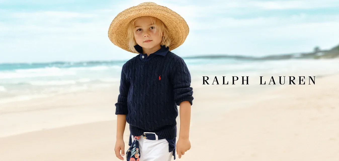 Marine-blaues Kabelstrickpullover, weiße hochgekrempelte Hosen und ein großer Strohhut. Ausgestattet mit einem blumengemusterten Schal, der um die Taille gebunden ist.