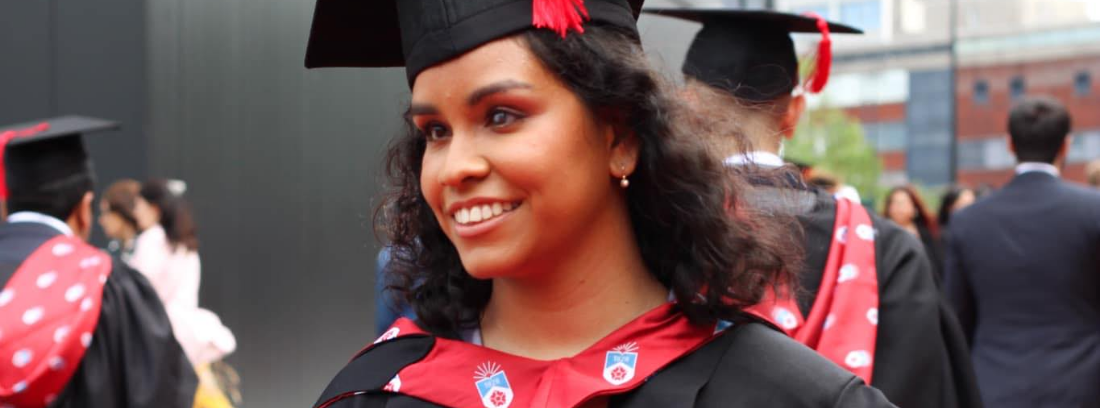 Jane smiling at her graduation ceremony, wearing a black and red gown and mortarboard.