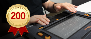 A person uses the Monarch. A badge highlights HumanWare’s inclusion among Forbes’ 200 recognized accessibility companies.