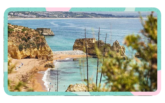 Turquoise and pink border shapes, elevated view, calm blue-turquoise ocean, distant hillside coastline, golden-tan sandy beach, ochre rust limestone cliffs, three weathered wooden poles, beachgoers and green pine branches foreground.