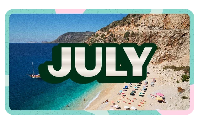Turquoise and pink border shapes, 'JULY' white bold text on dark green rounded rectangle, aerial view, clear blue sky, deep blue to turquoise ocean gradient, tan beige reddish-brown rocky cliffs, crescent sandy beach, beachgoers, colourful umbrellas, red orange blue, small sailboat and green vegetation.