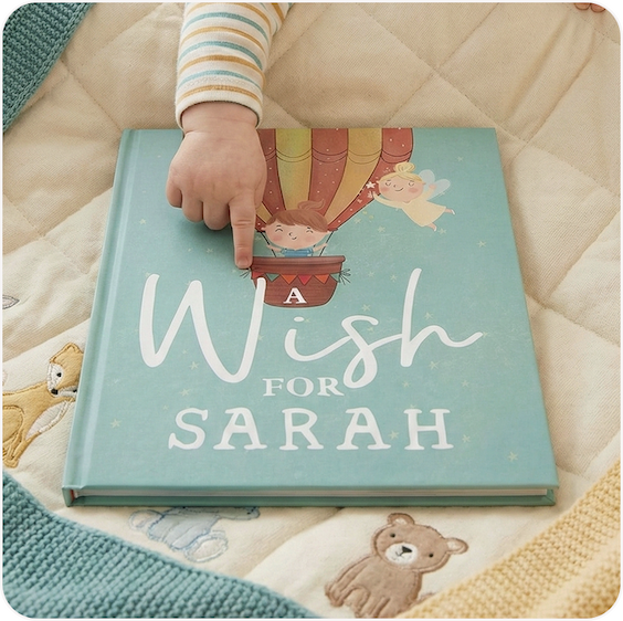 A personalised children's wish book with the name Sarah on the cover, resting on a soft quilted blanket alongside a teddy bear
