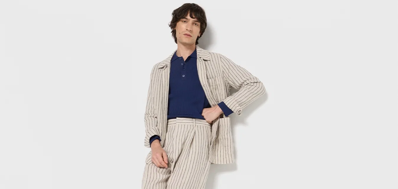 Gestreepte beige colbert over een blauwe polo, gecombineerd met gestreepte broeken en zwarte schoenen. Glad stof met verticale lijnen en een accent van zak.