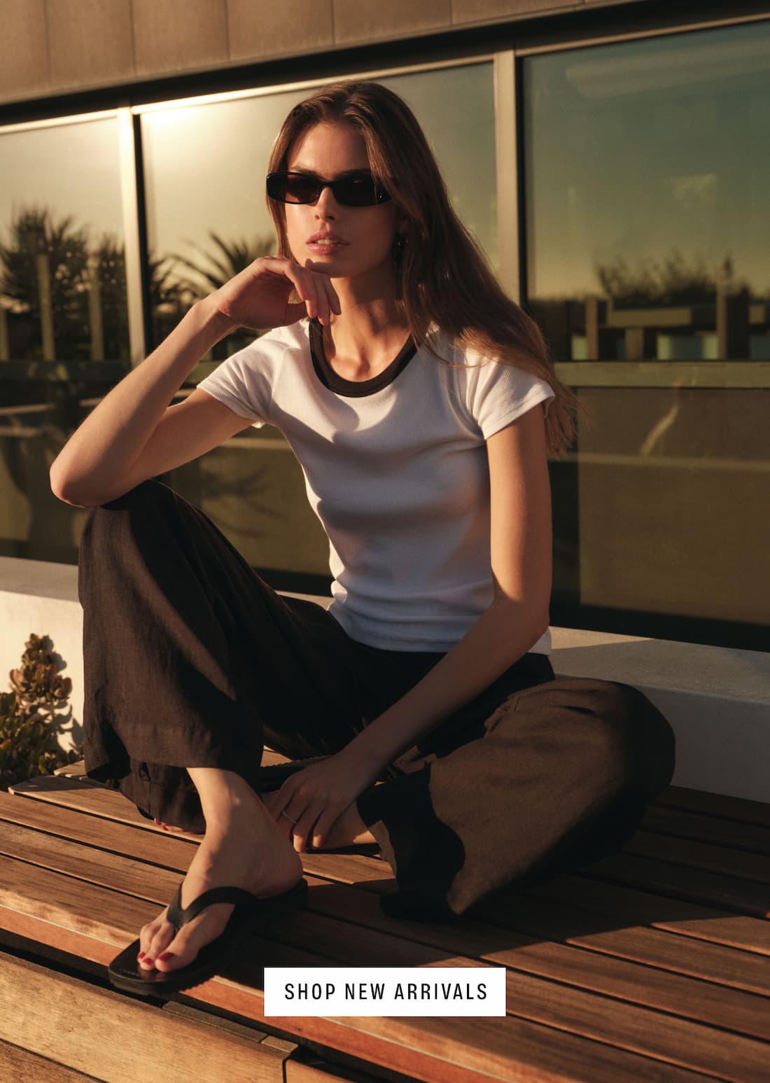 A woman sits on a porch in the sun. Featuring the Miley Tee.