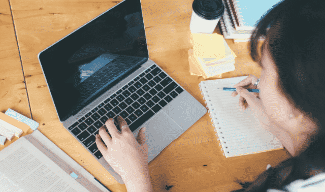 A professional genealogist working on a laptop computer and taking notes.