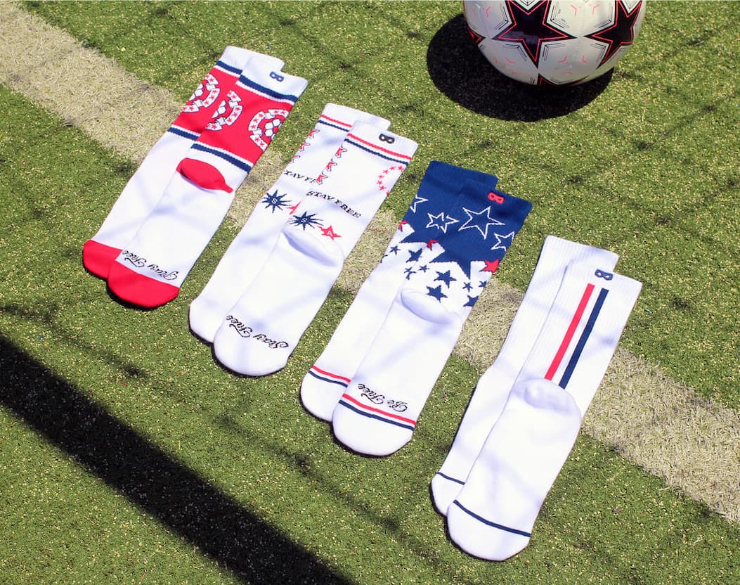 USA 250 Crew Socks laid next to a soccer ball under a goal 