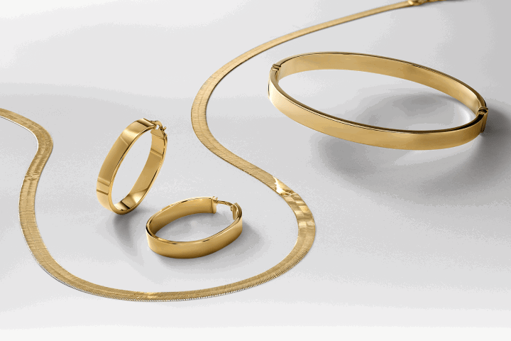 Sleek yellow gold necklace, hoop earrings, and bangle bracelet displayed together.