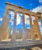 Ancient Greek temple columns rising against a bright blue sky with scattered clouds