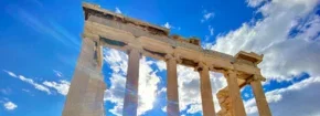 Ancient Greek temple columns rising against a bright blue sky with scattered clouds