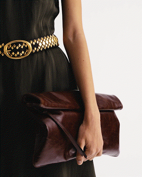 GIF of a model in a green dress and gold belt walking.