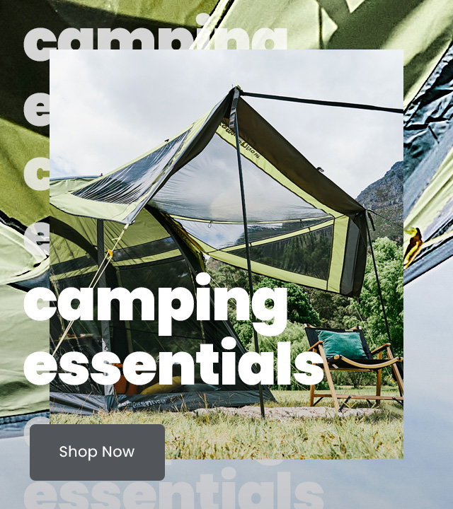 Green multi-room camping tent pitched on grassy ground with mesh panels and an extended canopy, set against a sunny hillside landscape with trees and mountains in the background. A folding camping chair sits to the right of the tent. Large overlaid text reads “Camping essentials.”