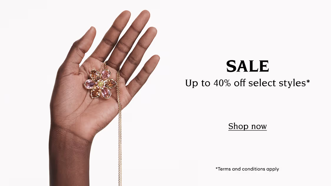 Hand holds a Swarovski necklace. Text reads “SALE Up to 40% off select styles* *Terms and conditions apply”. Clickable button reads “Shop now”