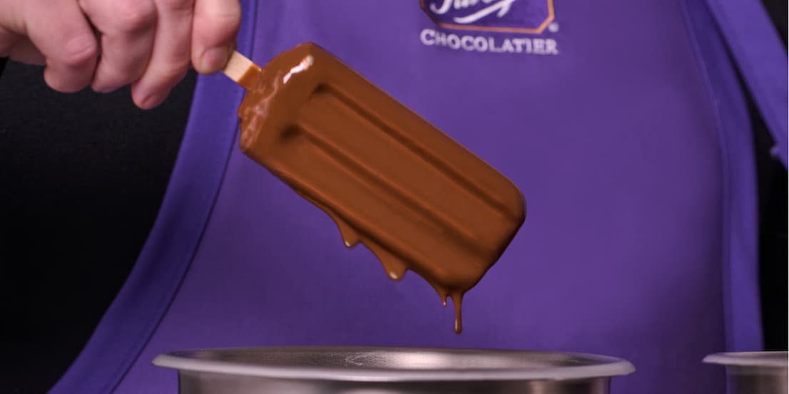 A shop staff's hand holding a hedgehog dip ice cream bar
