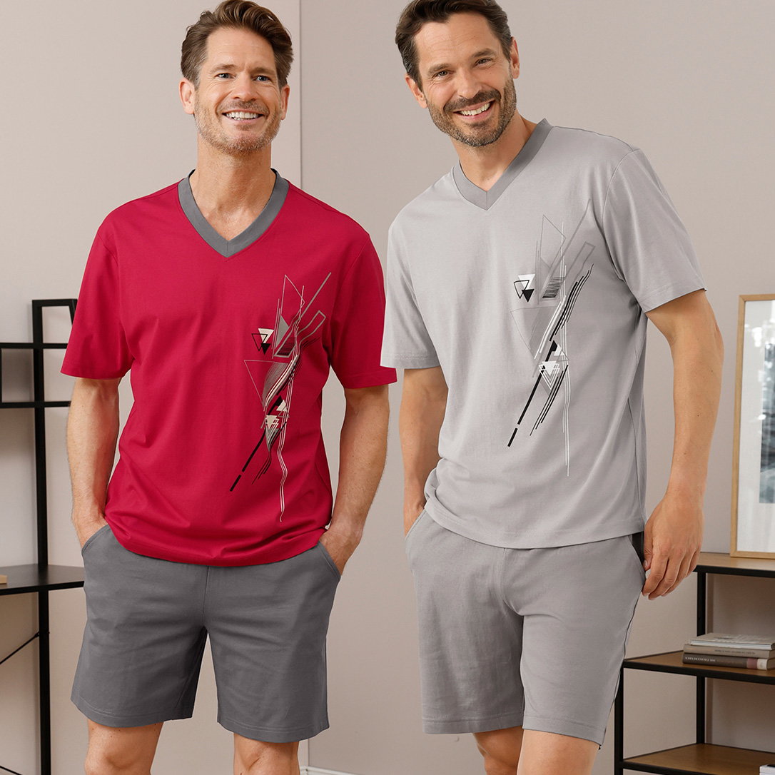 Zwei männliche Models tragen kurzärmelige V-Neck Shirts mit abstraktem Muster, eines in Rot mit grauem Kragen, das andere in Grau, dazu graue Shorts, stehen in einem modernen Raum.