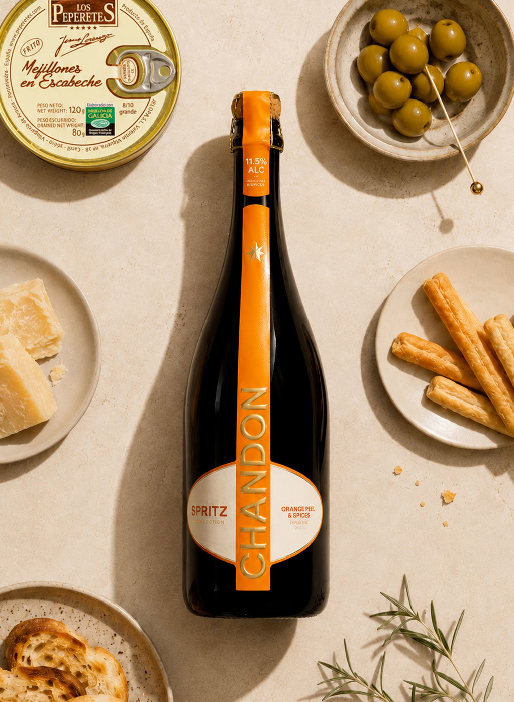 Chandon Spritz bottle with orange label surrounded by green olives, cheese, breadsticks, crackers and a tin of mussels