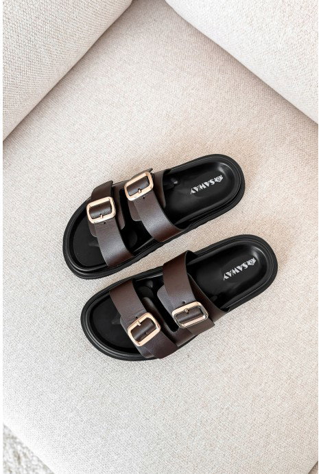 Pair of brown leather double-strap sandals with gold buckles on a beige fabric sofa, top-down view