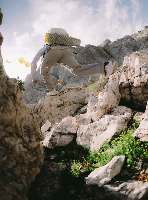 A hiker scrambling up rocks in his Peak Rambler™ Pants.