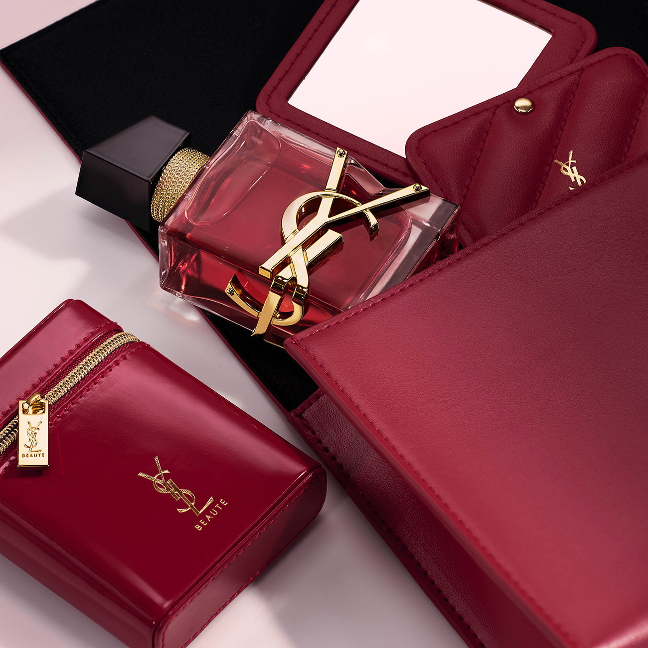 A bottle of YSL Libre fragrance surrounded by matching cherry-red leather beauty cases, a mirror, and accessories.
