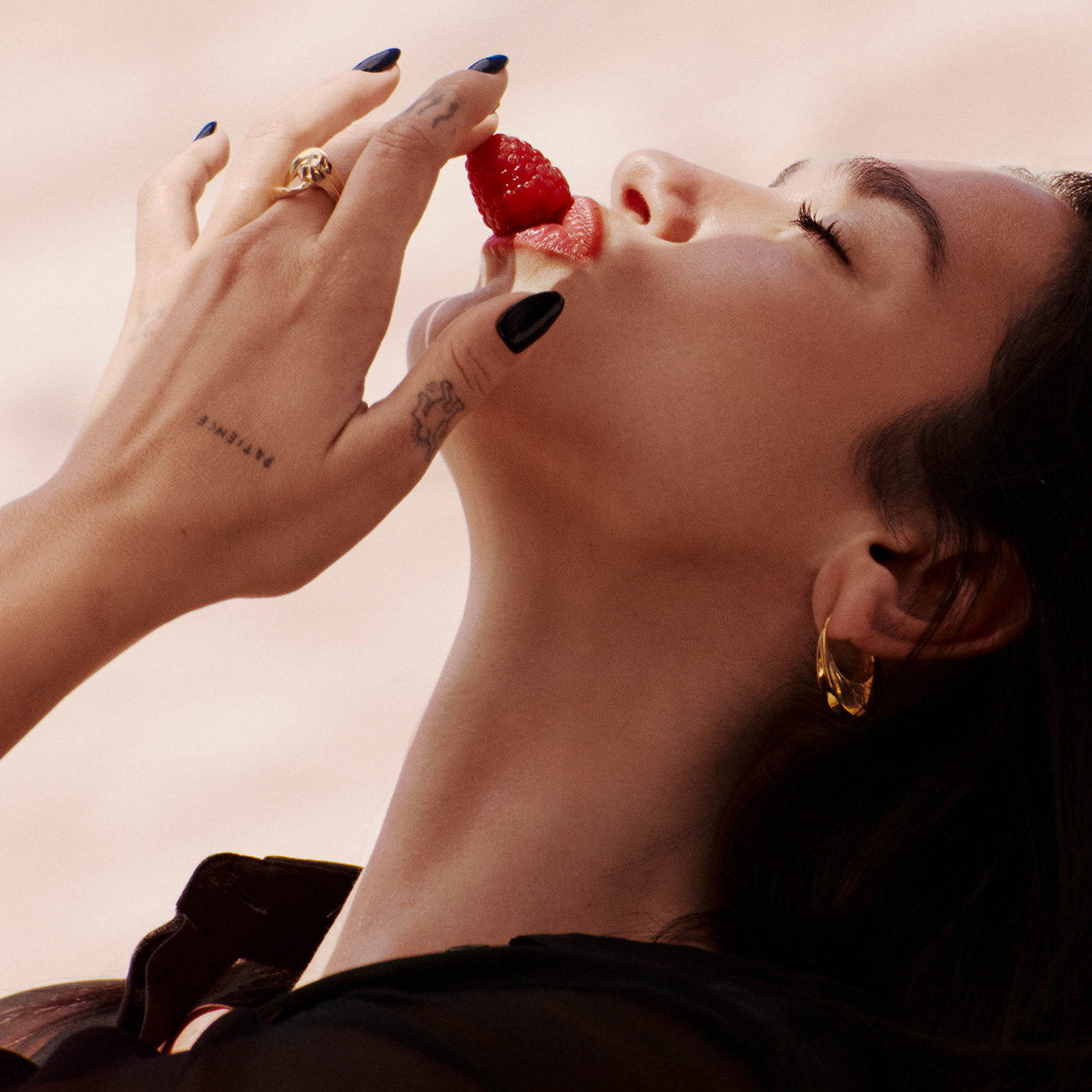 Singer Dua Lipa close-up as she gently places a fresh raspberry on her red lips.