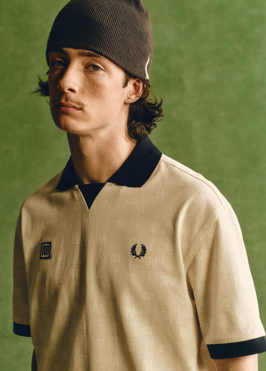A close up of a male model wearing a Fred Perry x MEYBA Printed Polo Shirt in Ecru