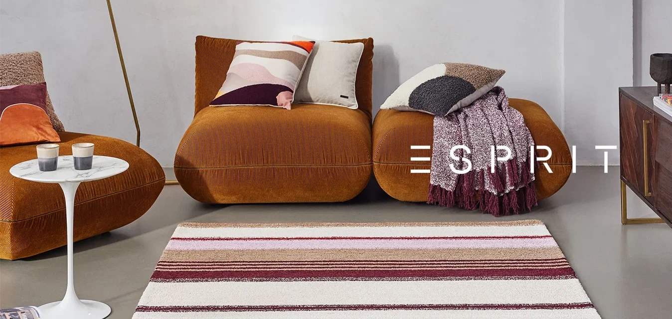 Braune Kord sofa mit bunten Kissen, ein weißer Marmor-Beistelltisch, ein gestreifter Teppich in Rot und Beige sowie eine schwarze Stehlampe.