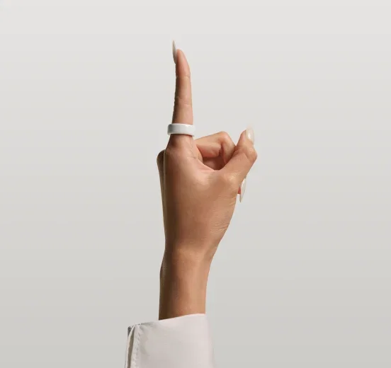A hand with one finger pointed upward wearing an Oura Ring 4 in Cloud against a light gray background.