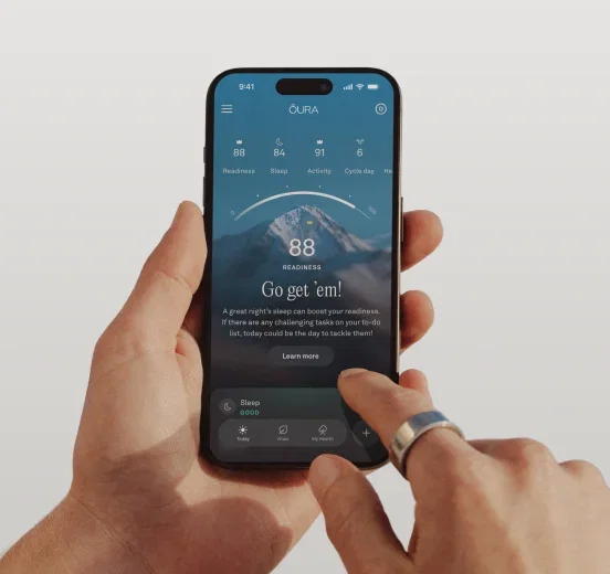 Hand holding a smartphone displaying the Oura app readiness score of 88, with an Oura Ring 4 worn on the index finge