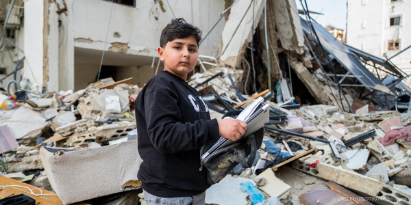 A young boy stands in front of rubble. 